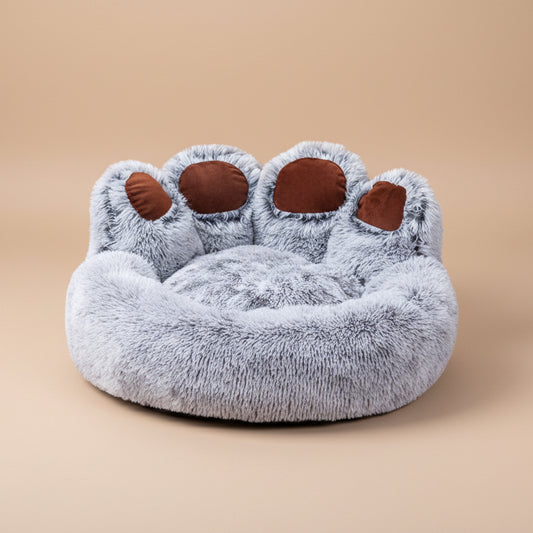 Plush paw-shaped pet bed with gray fur and brown pads on a white background