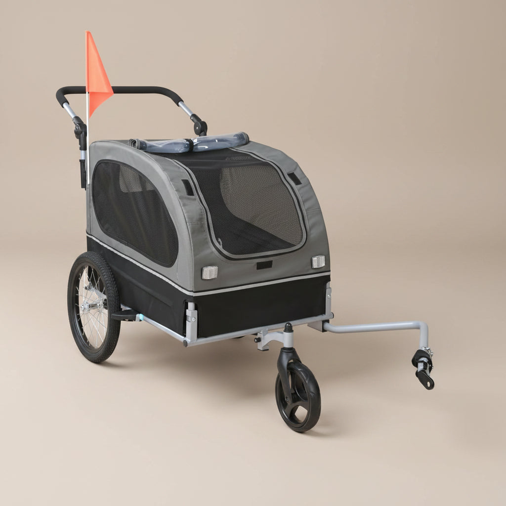A gray and black pet stroller trailer with mesh windows, a silver metal frame, a small orange flag, and a hitch for towing, shown on a plain white background.