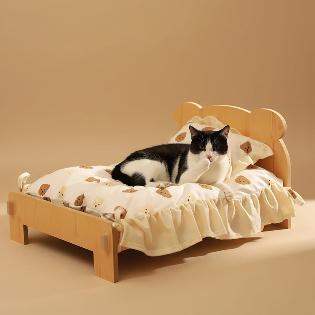 Tuxedo Cat lying on a small wooden bed, licking it's paw with a teddy bear pattern blanket on a beige background.