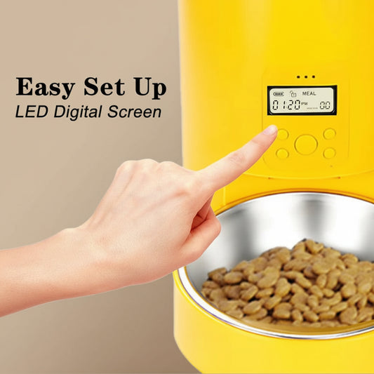 Yellow pet feeder with digital screen and a hand pointing to it, on a beige background.