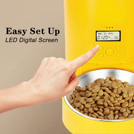 Yellow pet feeder with digital screen and a hand pointing to it, on a beige background.