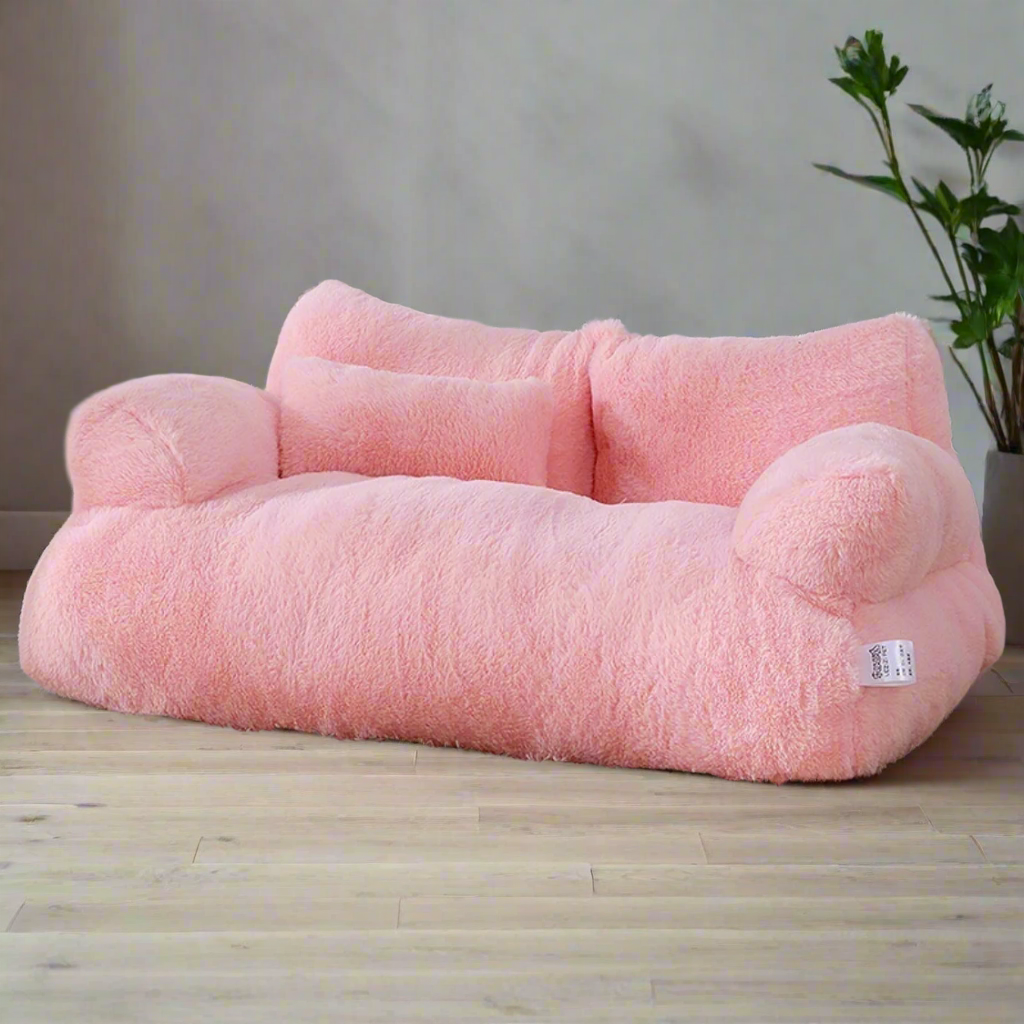 Pink pet bed on a carpeted floor with a lamp and decorative items in the background