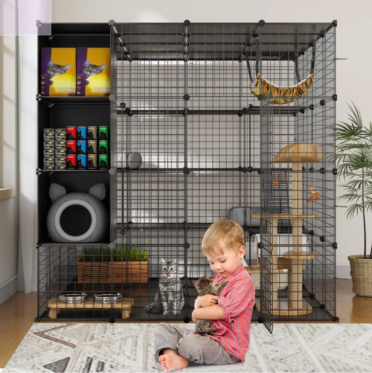 Child holding a cat next to a large black pet cage with various accessories in a room.