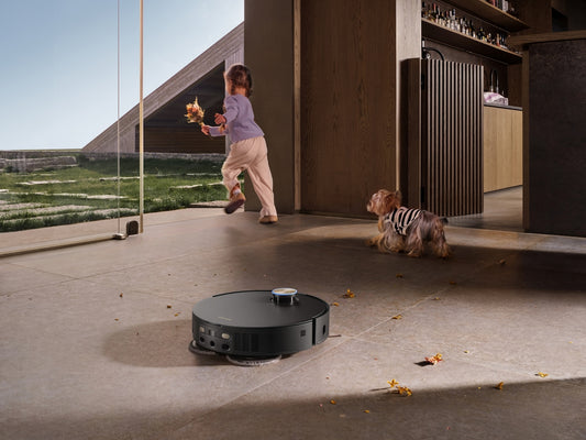 A girl and dog watch a robot vacuum cleaner.