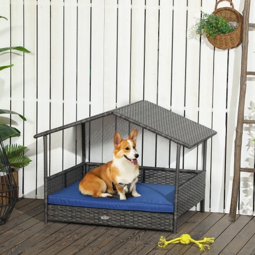 Dog sitting on a blue cushion in a wicker pet house on a wooden deck.