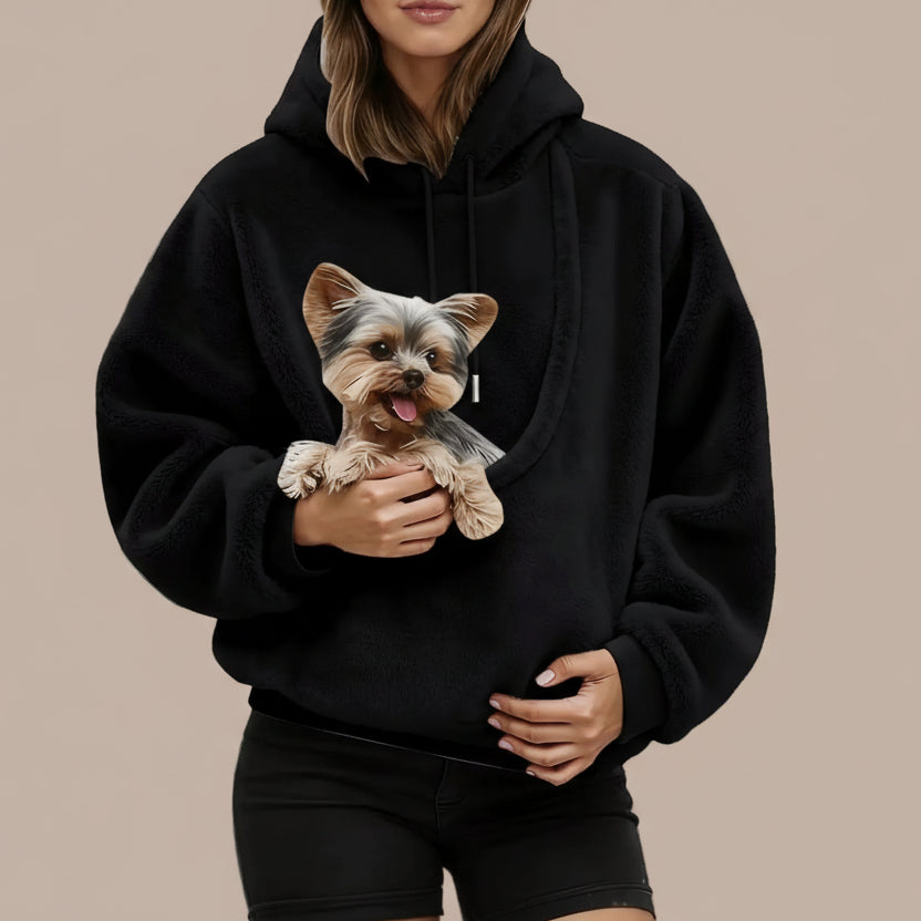 Person wearing a black hoodie with a dog design, holding a small dog.