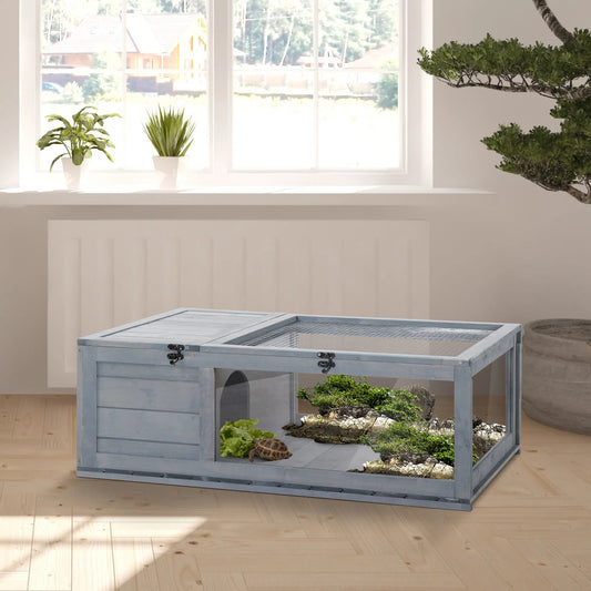Large terrarium with plants and small animals on a wooden floor, near a window.