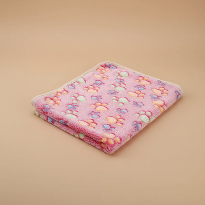 Pink pet blanket with colorful paw prints on a beige surface