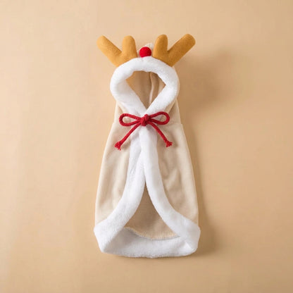 A soft cloak styled like a reindeer, featuring a beige body, white faux-fur trim, tan reindeer antlers, and a red nose and red bow, displayed on a light tan background.