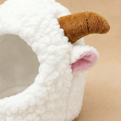 Close-up of a white plush sheep-shaped pet bed with a brown horn and pink inner ear on a white background.