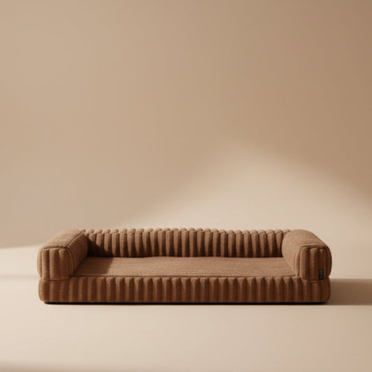 Brown plush dog bed in a bright room with a window and plant.