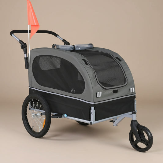 A pet stroller trailer with a gray fabric body, black mesh windows, a silver frame, black wheels, and an orange safety flag, shown on a plain beige studio background.