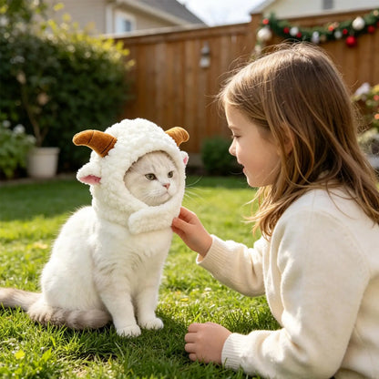 A white cat wearing a fluffy white sheep costume with brown horns sits on a green lawn while a young girl in a cream sweater gently pets it. A wooden fence and garden are visible in the background.