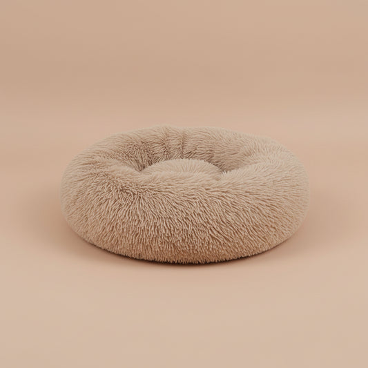 Fluffy beige pet bed on a white surface with a beige background