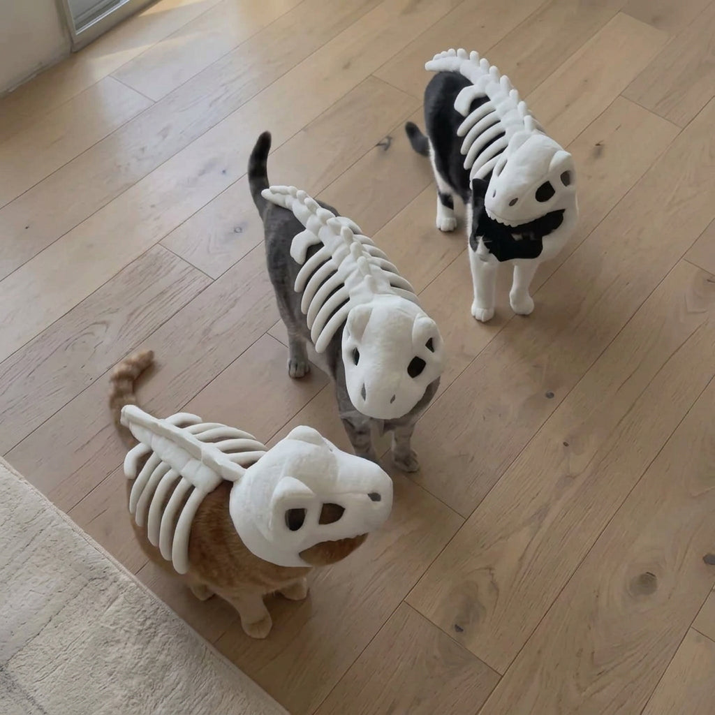 Three small cats wearing skeleton costumes standing on a light wood floor.