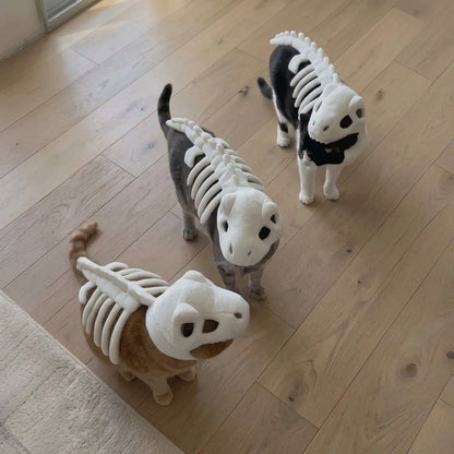 Three small cats wearing skeleton costumes standing on a light wood floor.