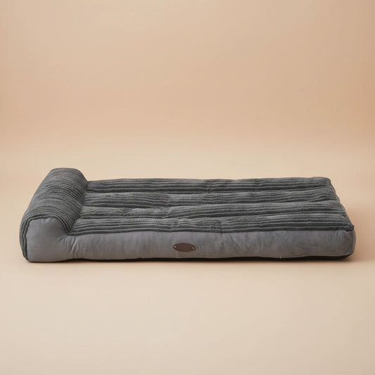 Dog lying on a large gray pet bed in a room with a window and curtains.