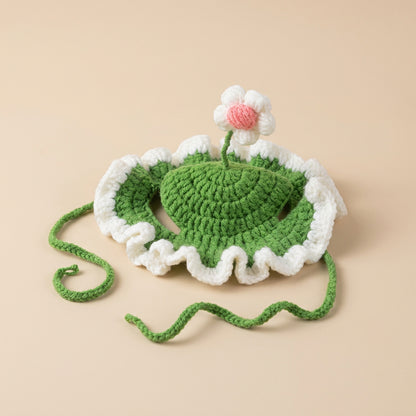 Crocheted green pet hat with a white flower and pink center on a light gray background