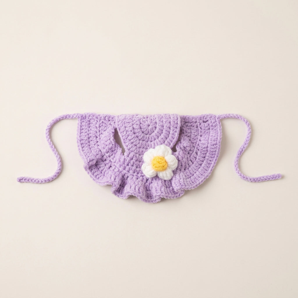 Purple crocheted cat hat with a white flower and yellow center on a light gray background