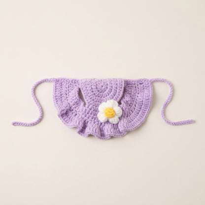 Purple crocheted cat hat with a white flower and yellow center on a light gray background